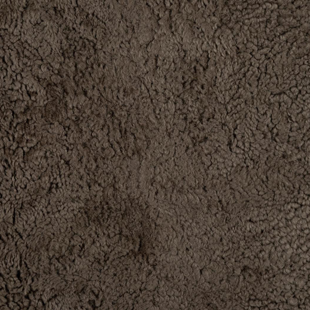 A close-up texture shot of dark brown sheepskin upholstery, with a dense, curly, and soft appearance.