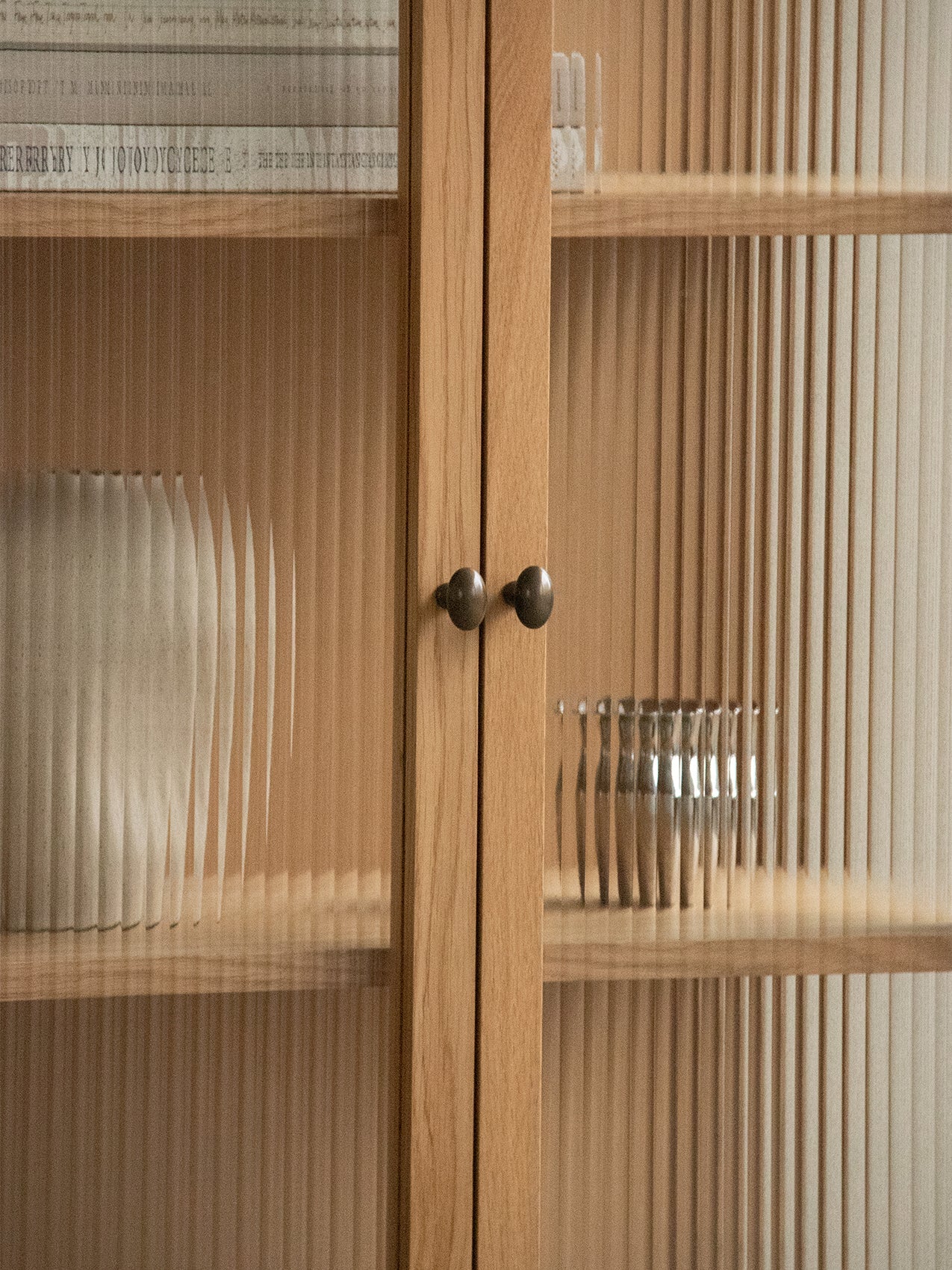 Close-up of the oak Curiosity Cabinet's reeded glass doors with brass handles. A vase and bowl are visible on the shelves.