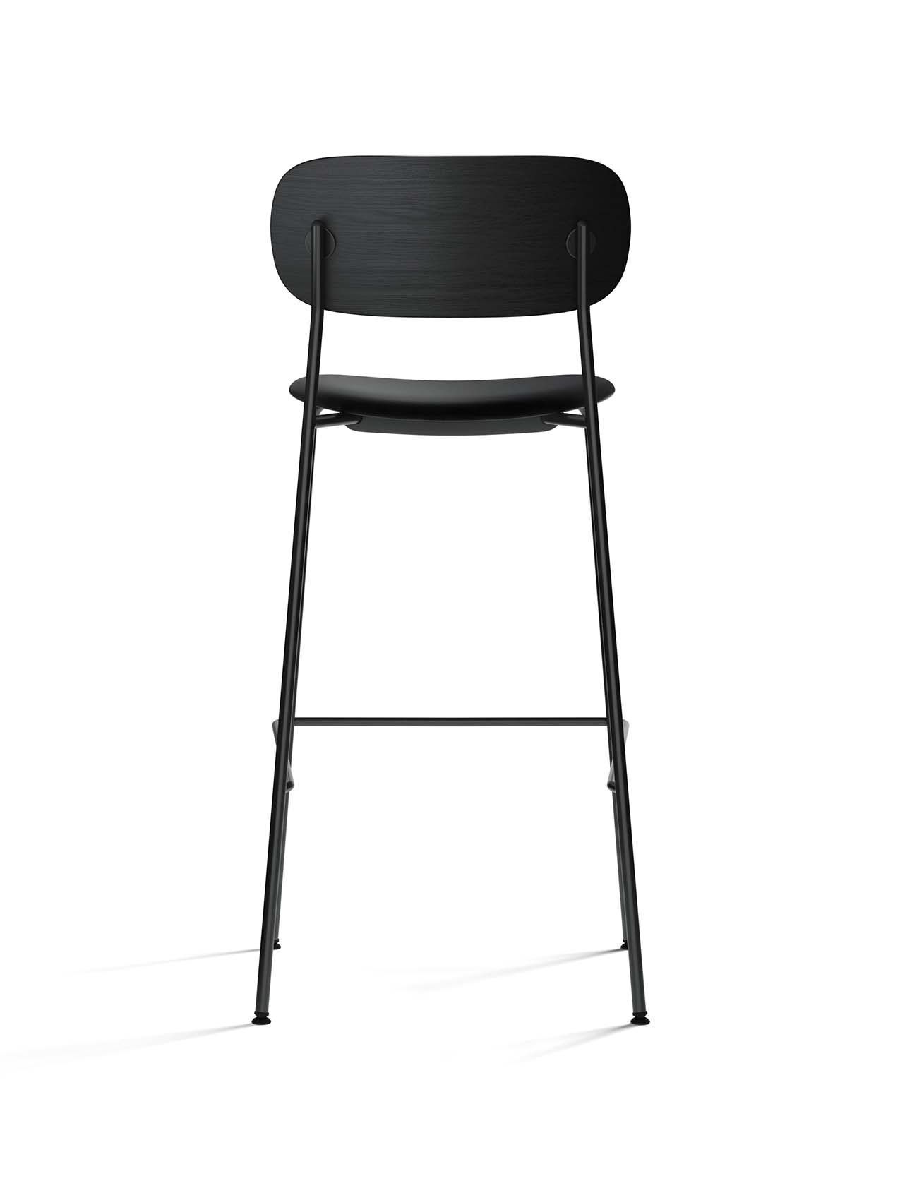 A tall, black Co Bar Chair from behind, with its black oak backrest, upholstered seat, and minimalist steel frame.