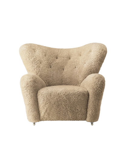 Front view of The Tired Man Lounge Chair in honey sheepskin. It features a curved, tufted back, plush arms and brass casters.