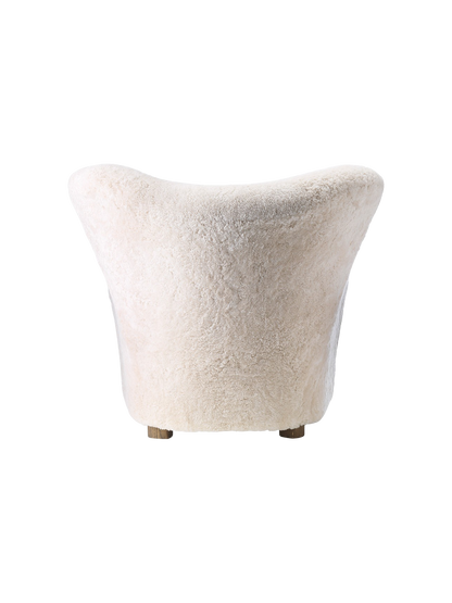 A back view of The Tired Man Lounge Chair, upholstered in plush, off-white sheepskin against a black background.
