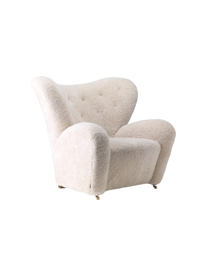 The Tired Man Lounge Chair, upholstered in off-white sheepskin, shown from a three-quarter angle against a black background.