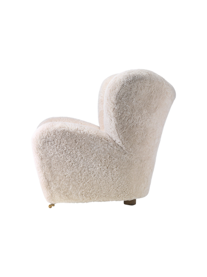 Side view of The Tired Man Lounge Chair upholstered in fluffy off-white sheepskin, showing its curved shape and wooden legs.