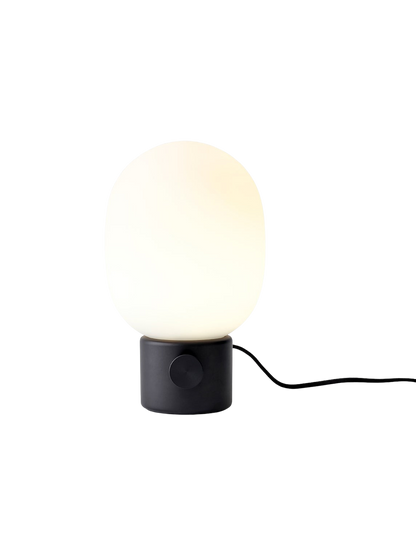 A front view of the JWDA Table Lamp, Small, in black painted steel with its illuminated white opal glass shade.