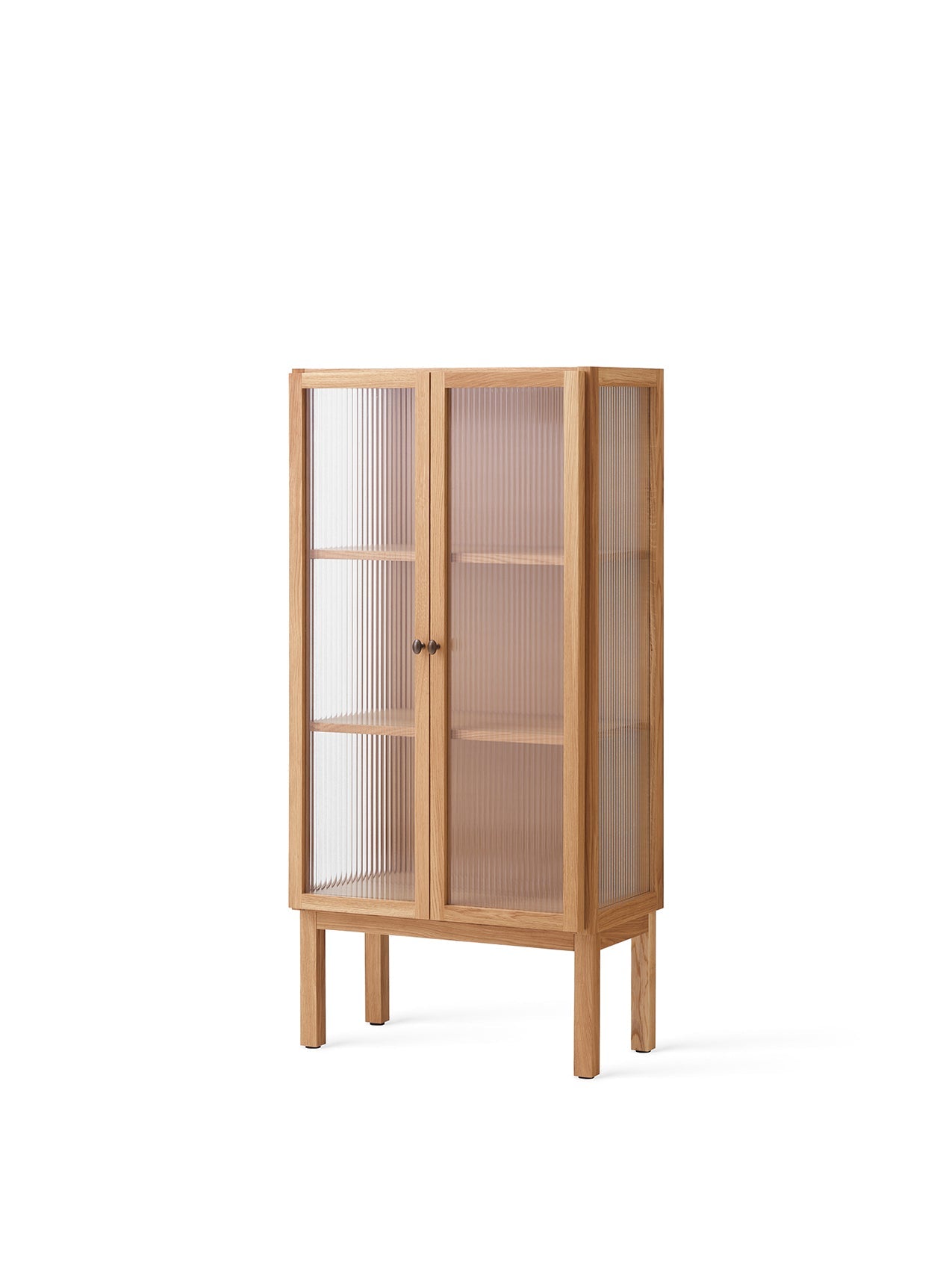 The tall Curiosity Cabinet in solid oak with reeded glass doors, seen from an angle. Internal shelves are visible inside.