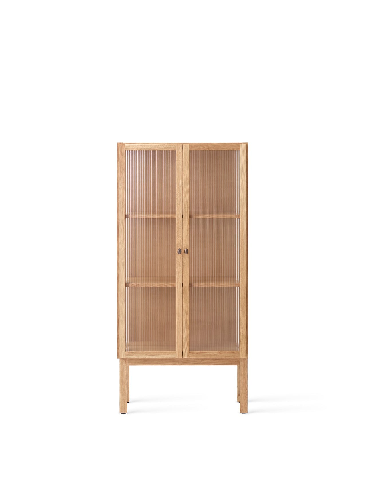 Front view of the tall oak Curiosity Cabinet. It has two reeded glass doors with small brass handles and stands on four legs.