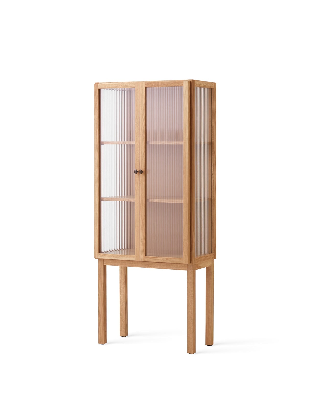An angle view of the tall solid oak Curiosity Cabinet, featuring two reeded glass doors and standing on four slender legs.