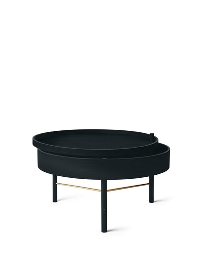 The round, black ash Turning Table, its top pivoted open to reveal storage. It has three legs with a brass accent bar.