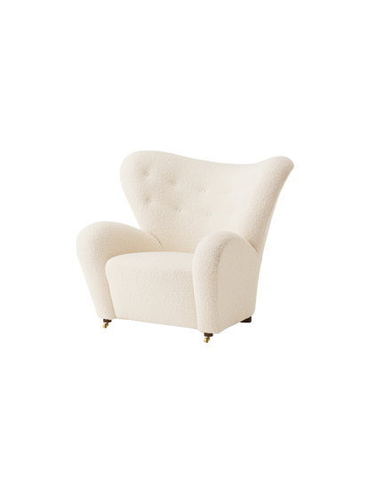 An angle view of The Tired Man Lounge Chair upholstered in a cream-coloured, textured textile against a black background.