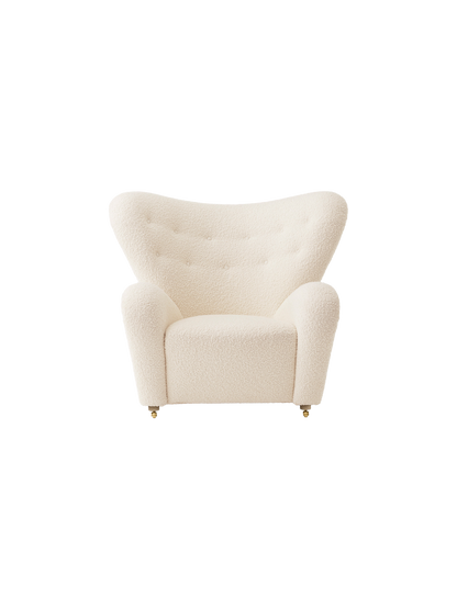 Front view of The Tired Man Lounge Chair in cream textile with a high, curved back, rounded arms and brass castors.