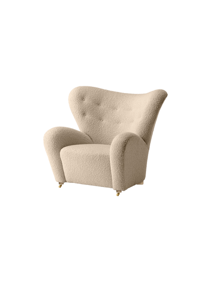 The Tired Man Lounge Chair upholstered in a cream textile, featuring a high curved back, tufted details, and gold castors.