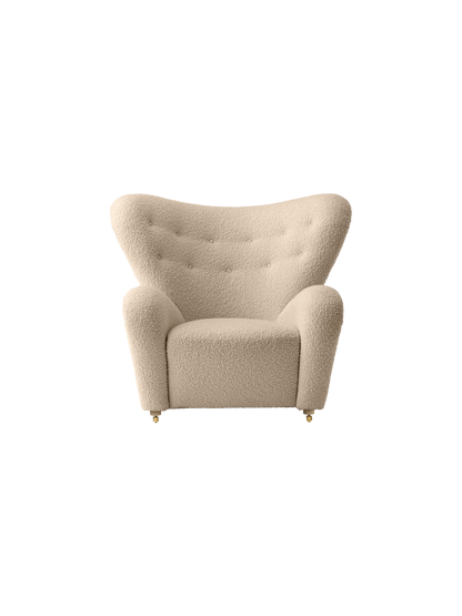 The Tired Man Lounge Chair, upholstered in a light, textured fabric with a tufted winged back and brass castors.