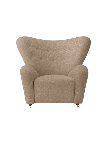 Front view of The Tired Man Lounge Chair upholstered in a textured beige textile, with a high curved back and brass castors.
