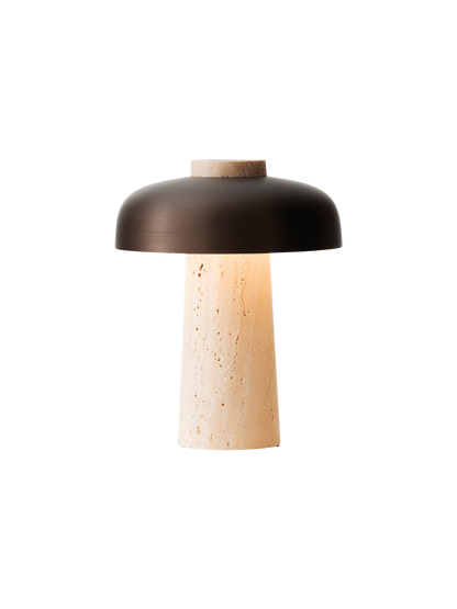 The Reverse Table Lamp, Portable, switched on, with a conical travertine base and a curved, bronzed aluminium shade.