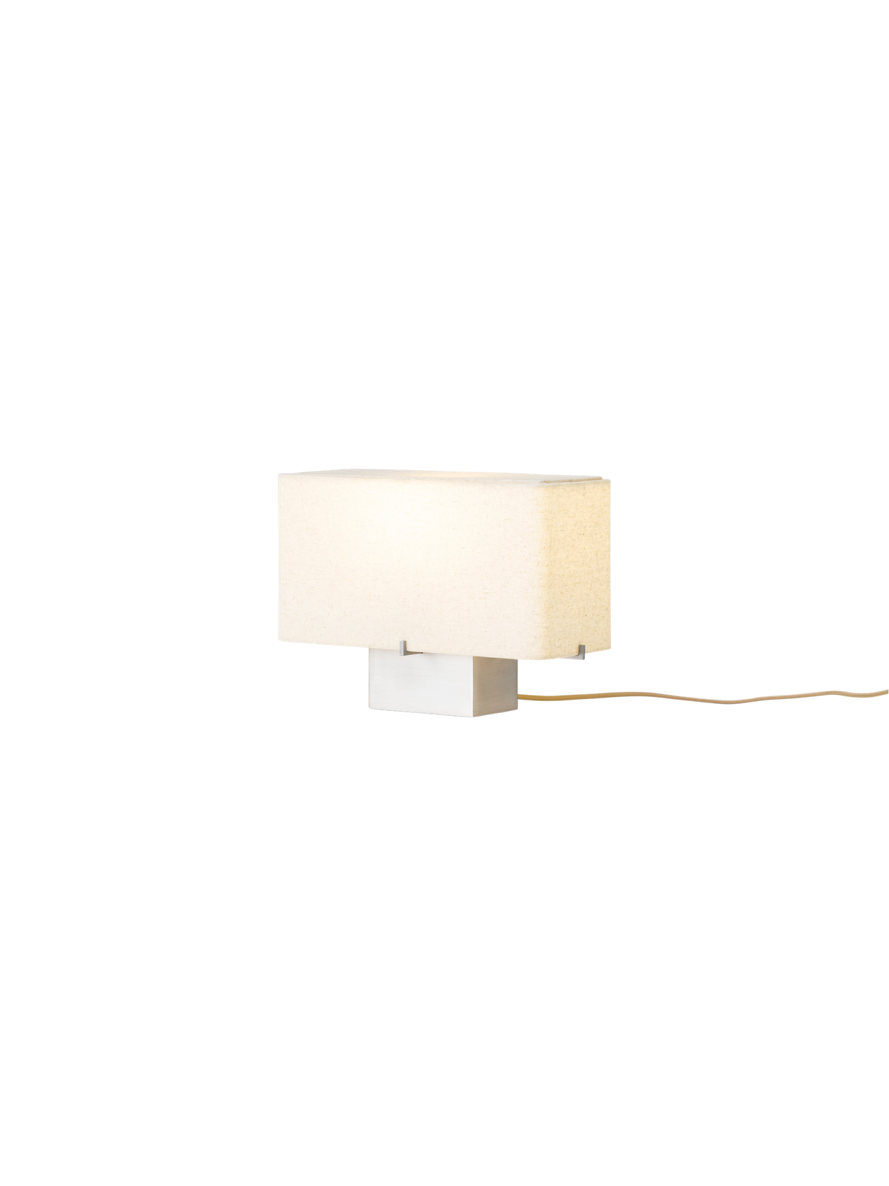 An angle view of the illuminated Nonna Table Lamp, featuring a rectangular sand-coloured textile shade on an aluminium base.