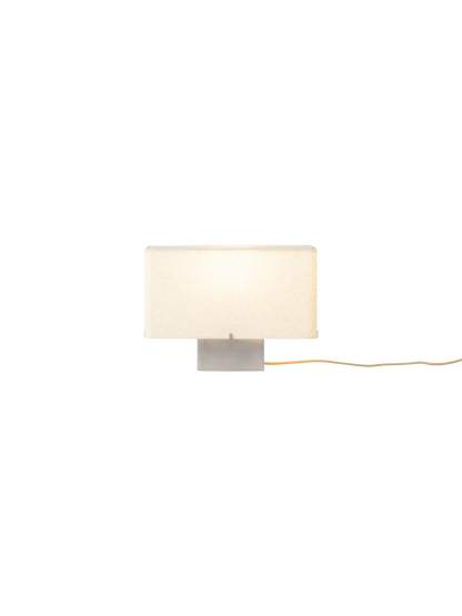 Front view of the illuminated Nonna Table Lamp with its rectangular, sand-coloured shade and brushed aluminium base.