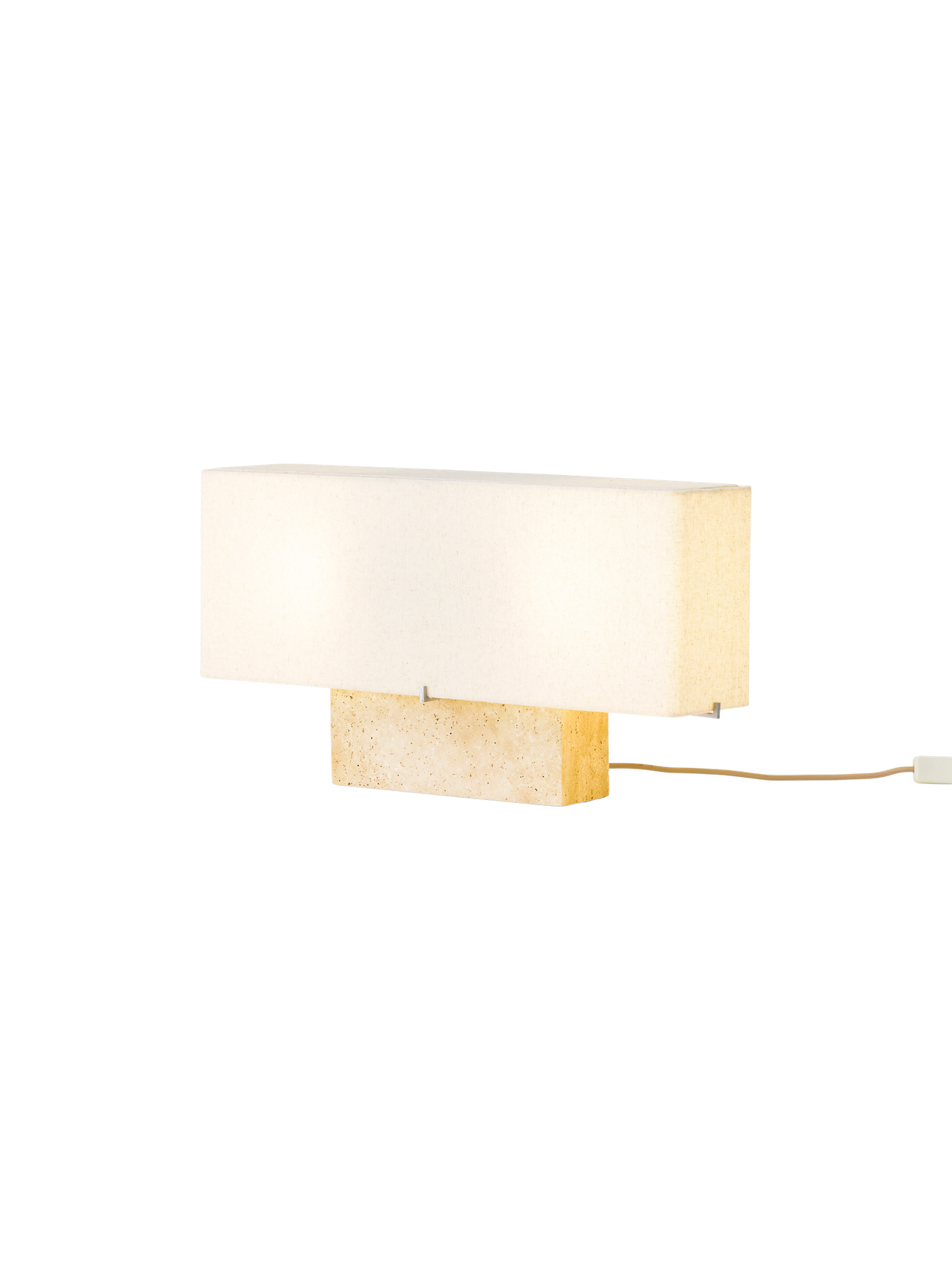 Angled view of the Nonna Table Lamp in Travertine, illuminated to show its rectangular stone base and long, fabric lampshade.