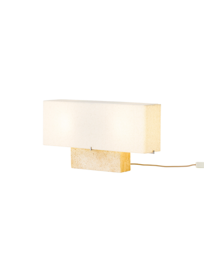 Angled view of the Nonna Table Lamp in Travertine, illuminated to show its rectangular stone base and long, fabric lampshade.