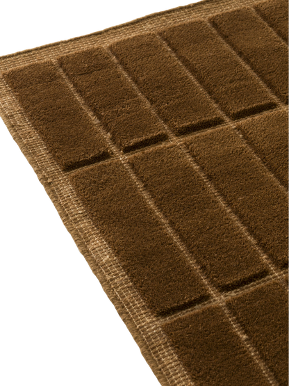 A close-up, detailed image of a brown woven textile with a geometric pattern of raised, plush rectangular sections.