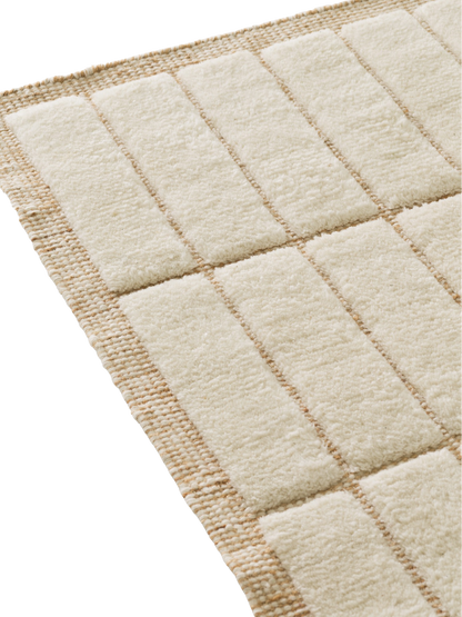 A close-up image showing the texture of a rug with a grid pattern of soft, cream-coloured pile and a flat, beige weave.