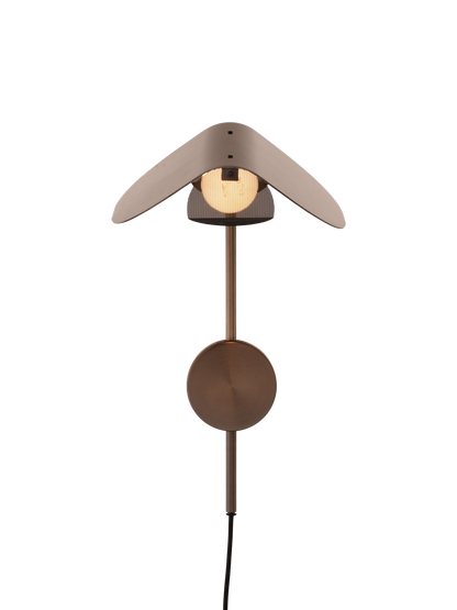 Front view of the turned-on Wing Wall Lamp in Bronzed Aluminium, featuring its wing-shaped shade over a glowing bulb.