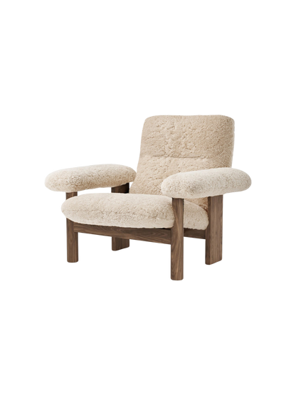 Angled view of the Brasilia Lounge Chair, featuring a high back and cushioned seat in natural sheepskin and a walnut frame.