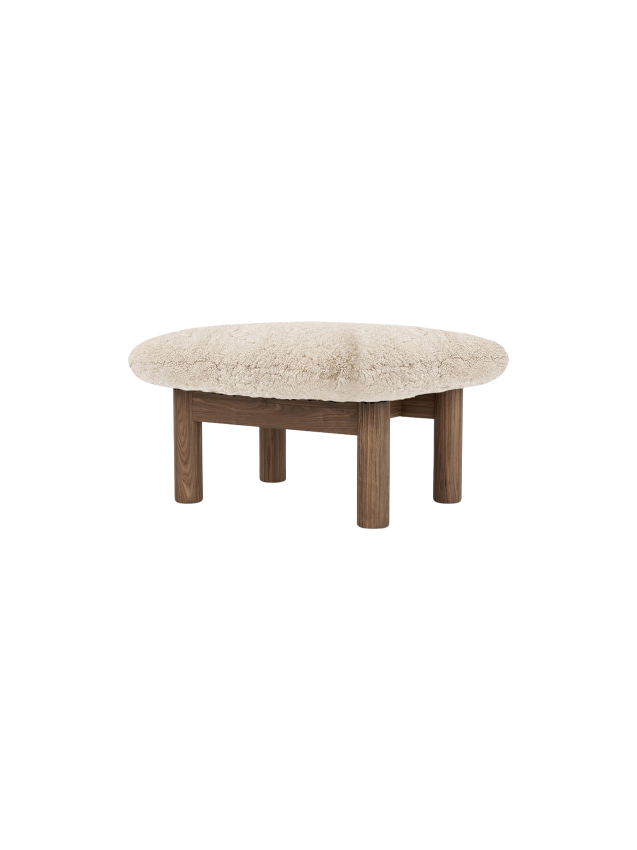 Angled view of the Brasilia Ottoman with a plush sheepskin cushion and four robust, cylindrical wooden legs.