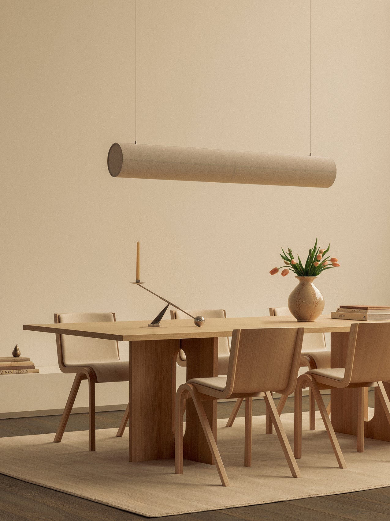A light oak Androgyne Dining Table and Ready Dining Chairs sit on a beige rug, illuminated by a Hashira Linear Pendant Lamp.