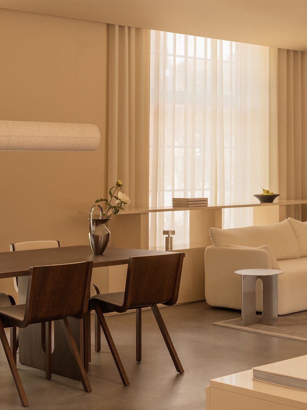A warmly lit dining room featuring the Androgyne Dining Table, Ready Dining Chairs, Offset Sofa, and Hashira Linear Pendant.