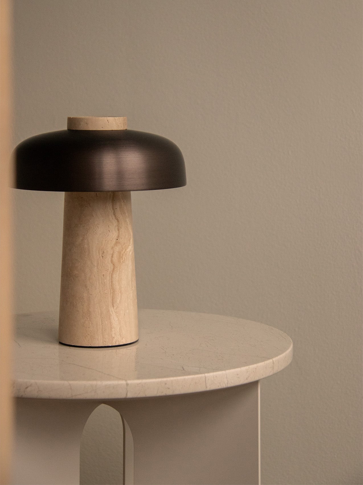 The Reverse Table Lamp, Portable, with its travertine base and bronzed shade, sits on a light-coloured Androgyne Side Table.