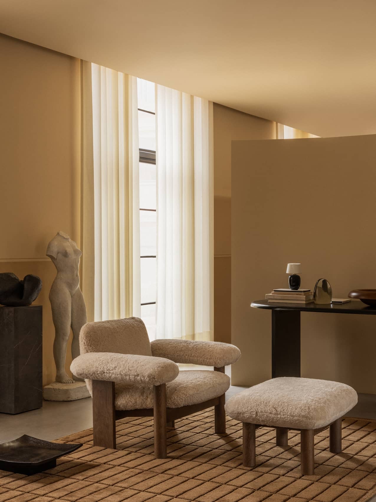 A Brasilia Lounge Chair and Ottoman on a Tile Rug. The room includes an Eclipse Desk, Torso Portable lamp, and a tall Plinth.