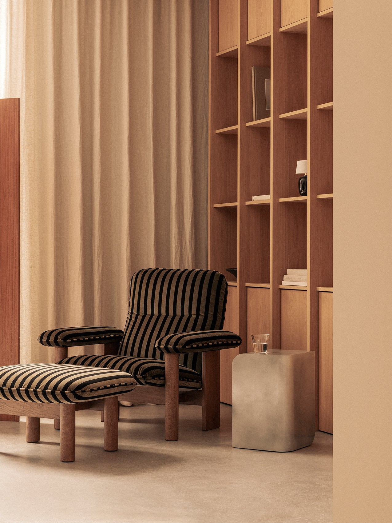 A black and beige striped Brasilia Lounge Chair and ottoman next to a Volume Side Table in front of a wooden bookcase.