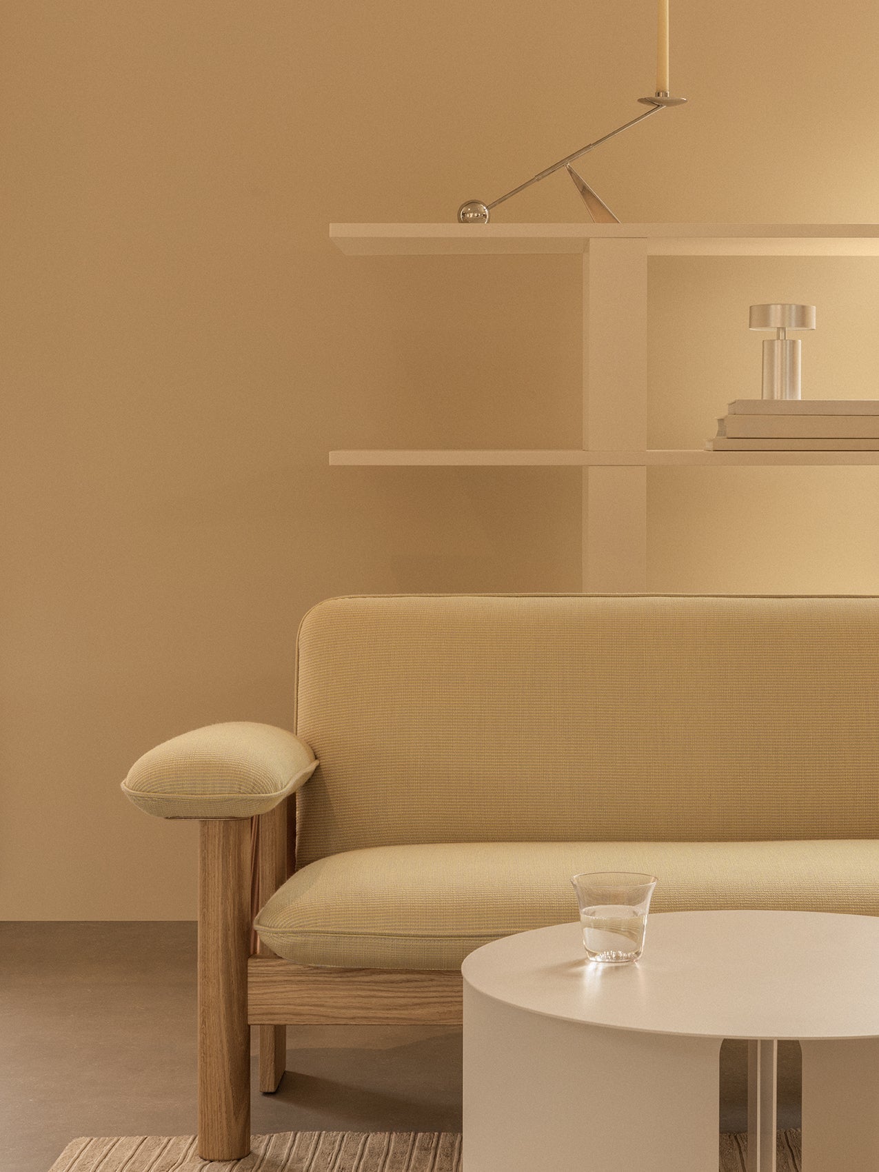 Yellow Brasilia Sofa with oak frame beside a white Androgyne Side Table. A silver Interconnect Candle Holder sits on a shelf.