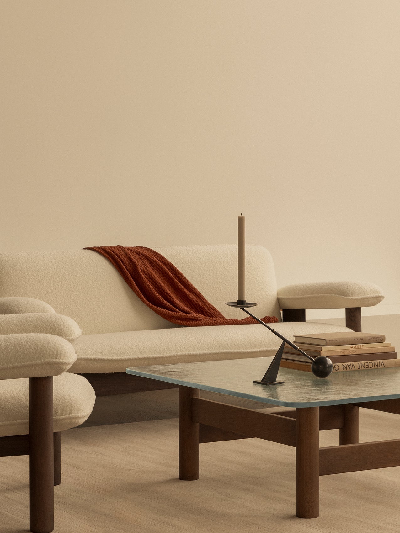 Cream Brasilia Sofa with a rust throw. In front, a glass Brasilia Lounge Table with an Interconnect Candle Holder and books.