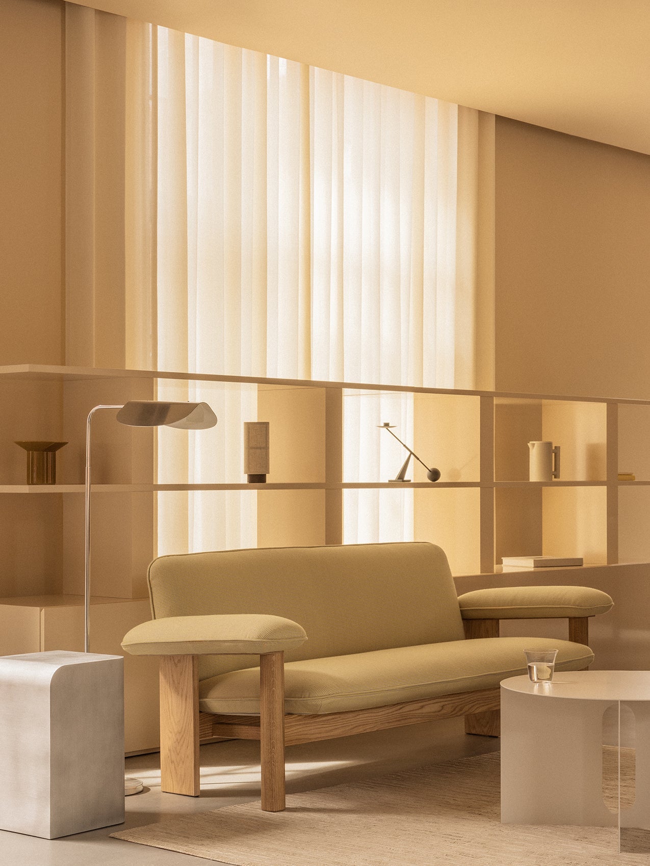 A warmly lit living room featuring the Brasilia Sofa in a light fabric, beside a Wing Floor Lamp and Androgyne Side Table.