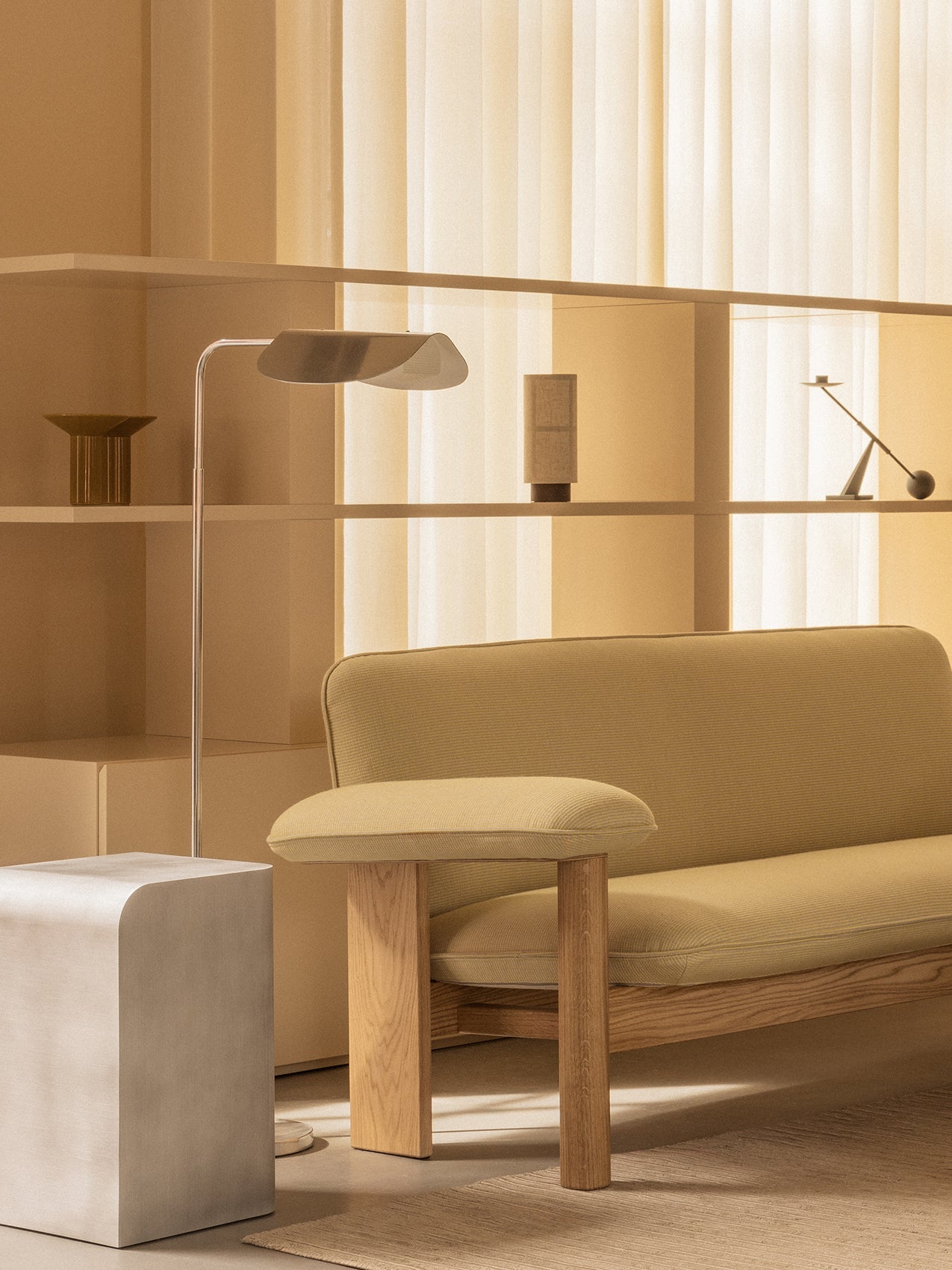 A warmly lit room with the Wing Floor Lamp, Brasilia Sofa, and Volume Side Table. On shelves, a Hashira Lamp and Interconnect