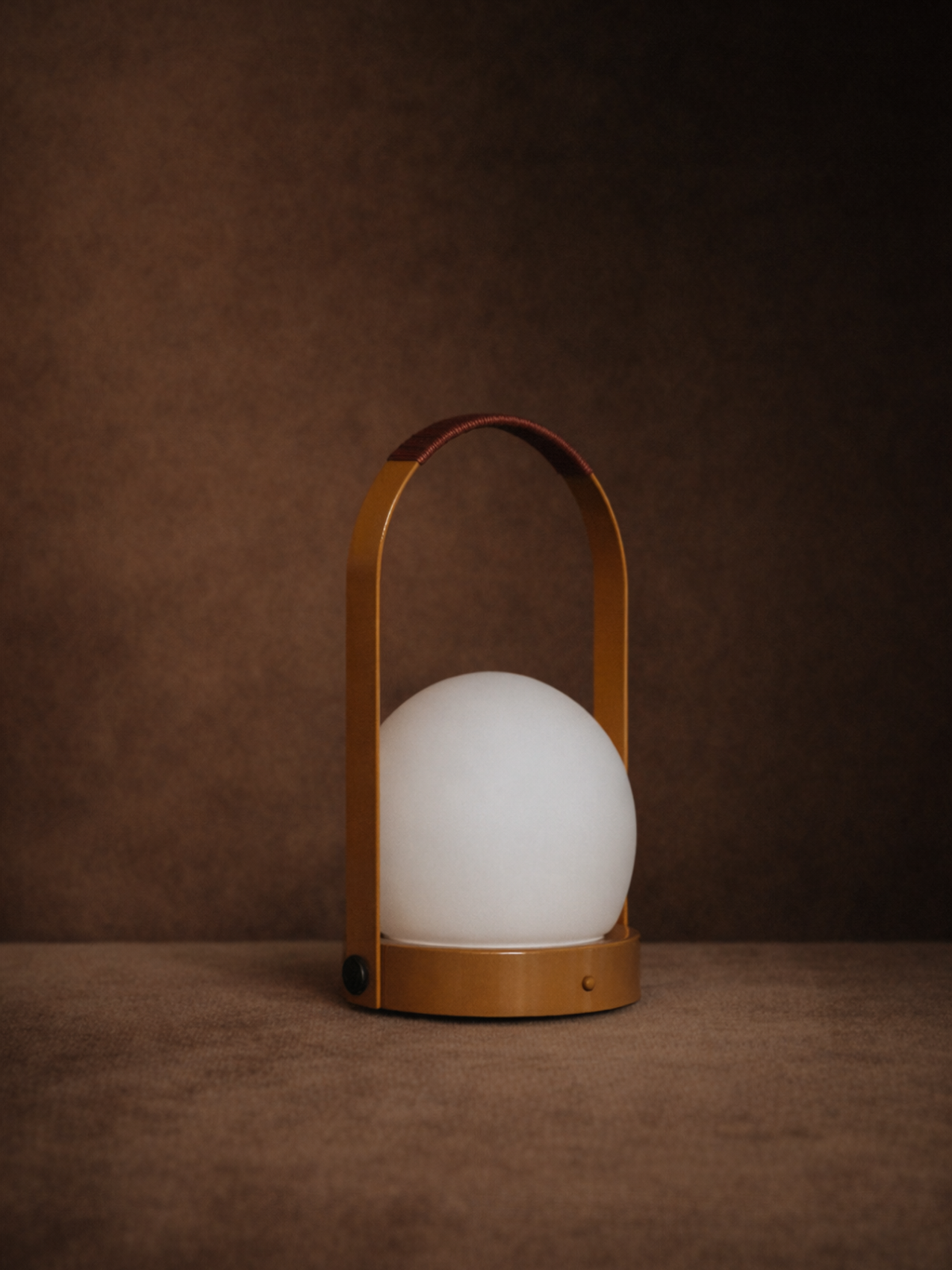 Carrie Portable Lamp in Golden Brown with a leather-wrapped handle and opal glass shade against a dark brown background.