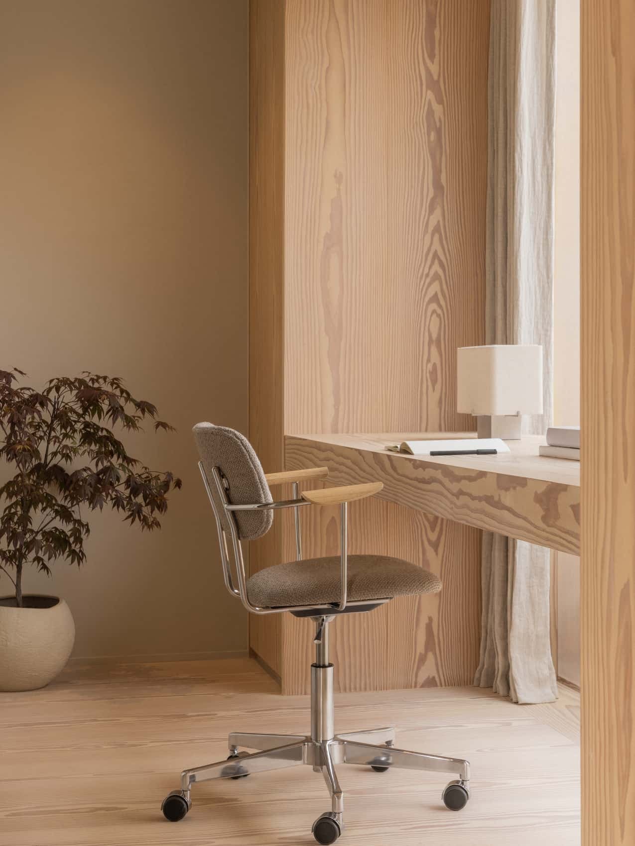 The Nonna Table Lamp on a built-in wood desk in a home office, with a brown upholstered Co Task Chair and a potted plant.