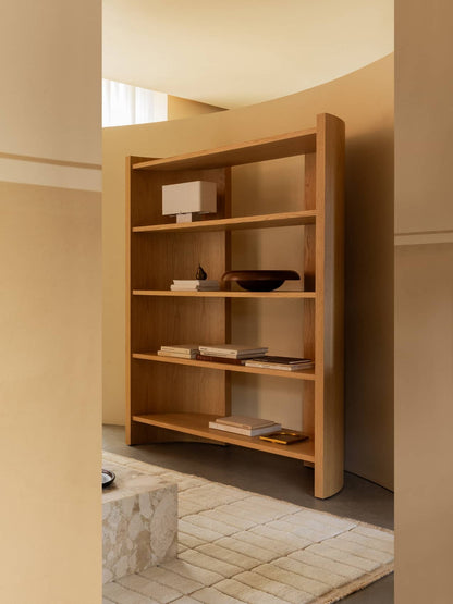 The Crescent Shelving H173 in oak, styled with a Nonna Lamp, Rond Bowl, and books, in a room with a marble Plinth Low table.