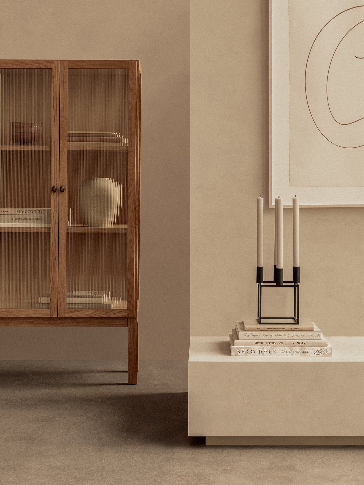 Oak Curiosity Cabinet with reeded glass doors next to a cream console with a Kubus 4 candle holder on a stack of books.