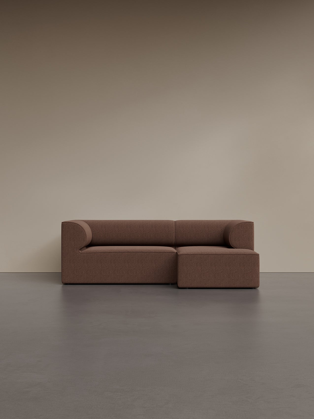 A brown Eave Modular Sofa, 86, 3-seater, Configuration 5, with a right chaise, against a beige wall on a dark grey floor.
