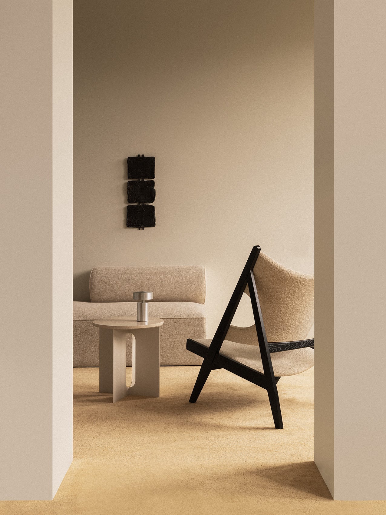 Side view of the Knitting Lounge Chair in black oak in a beige room with the Eave Modular Sofa and Androgyne Side Table.