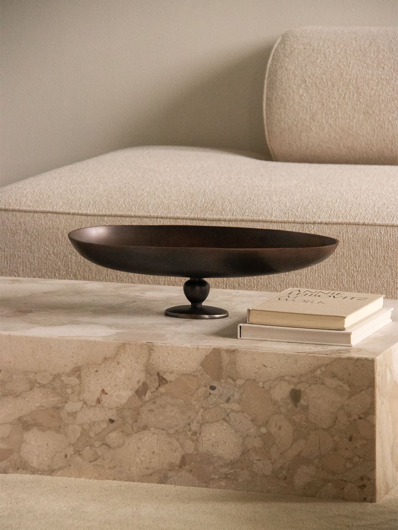 The dark bronze Pavot Centerpiece rests on a marble Plinth Low coffee table with a cream Eave sofa blurred in the background.