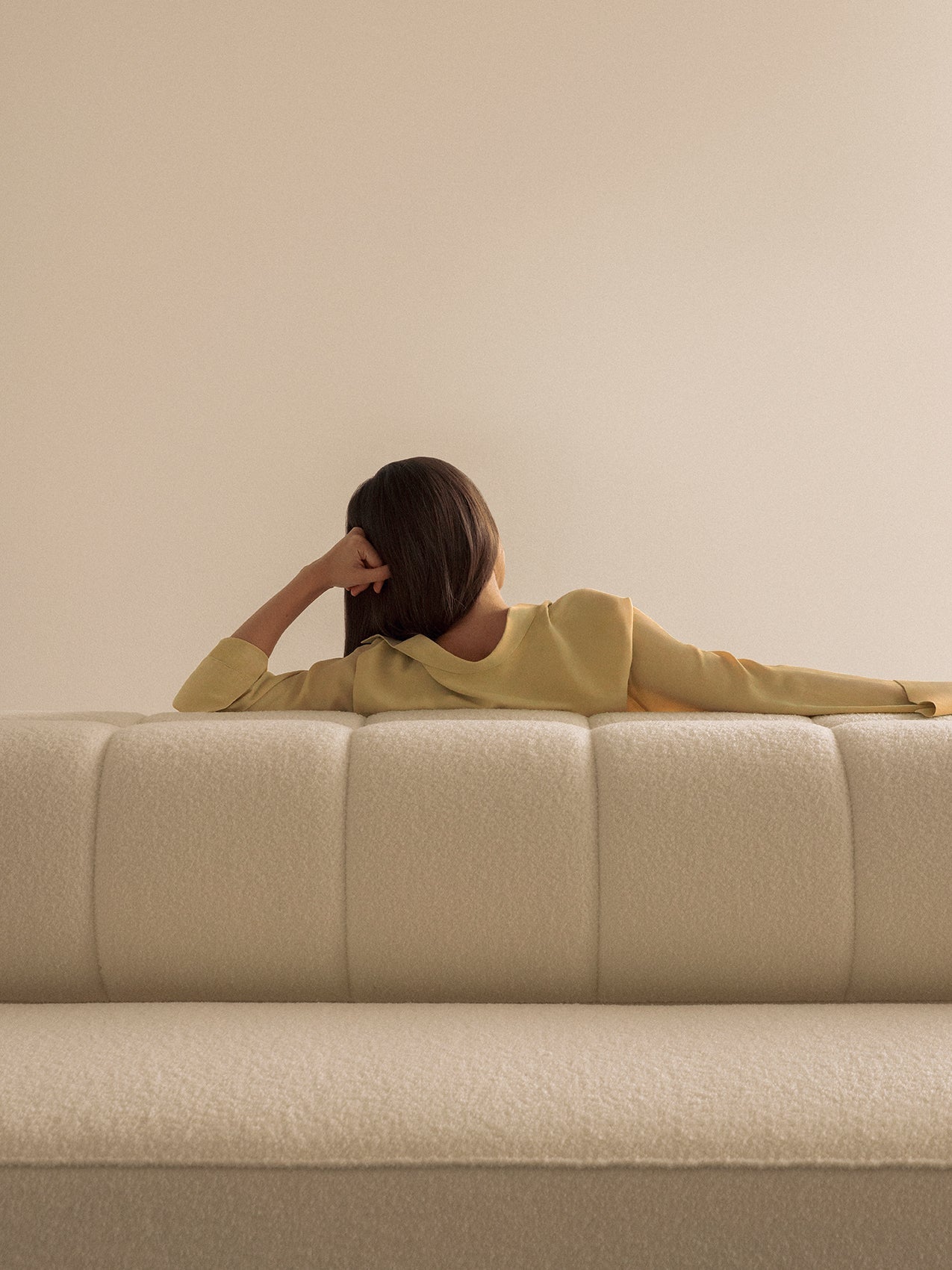 View from behind of a person in a yellow top lounging on the textured backrest of the Eave Seamline Modular Sofa 86.