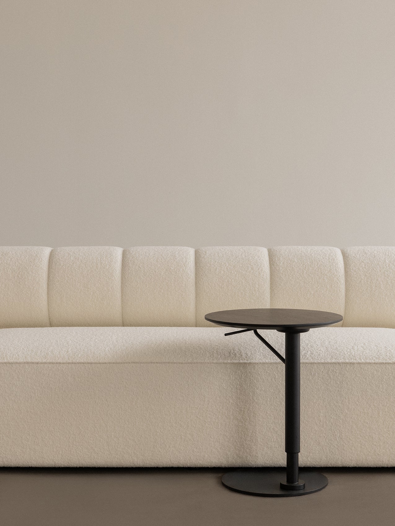 A close-up showing a black, round Branch Side Table next to the cream, bouclé upholstery of the Eave Seamline Modular Sofa.