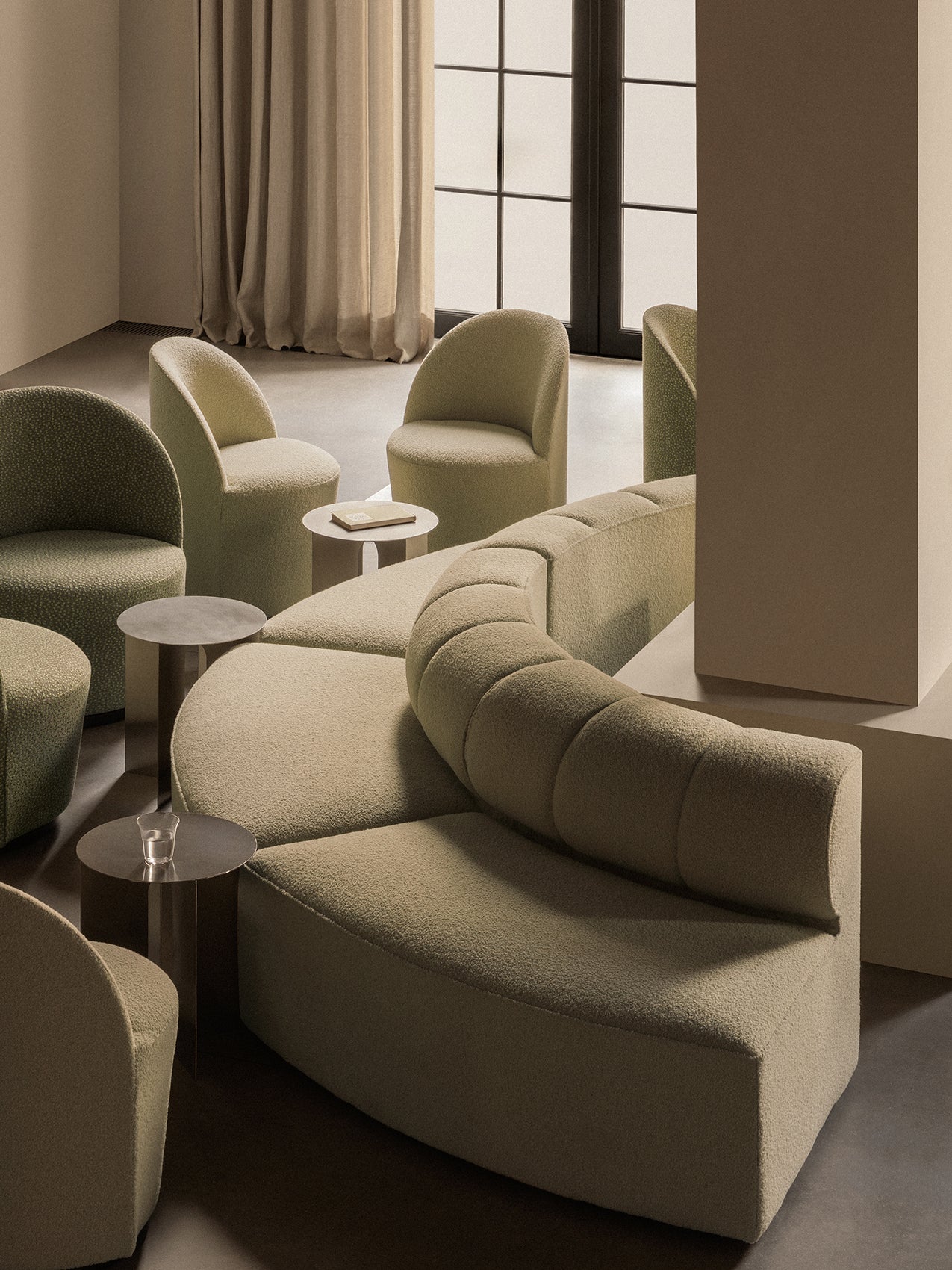 A lounge setting with a curved, beige Eave Seamline Modular Sofa, Tearoom Side Chairs and Androgyne Side Tables.