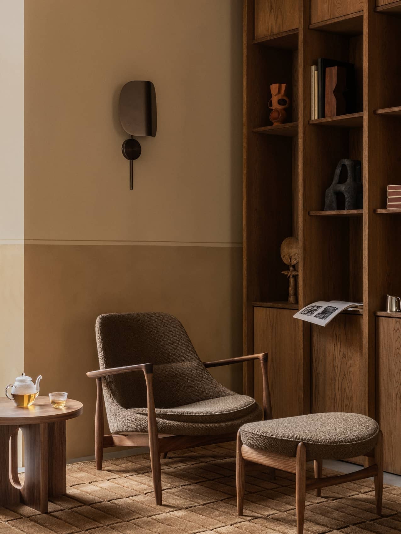 A living room featuring the Elizabeth Lounge Chair and Ottoman, Androgyne Side Table, Wing Wall Lamp, and a brown Tile Rug.