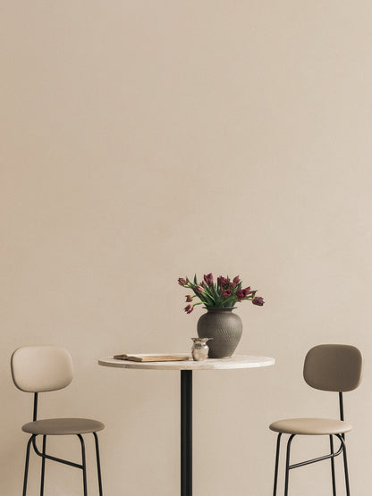 A Harbour Column Bar Table with a marble top, flanked by two beige Afteroom Bar Chairs. A vase of tulips decorates the table.