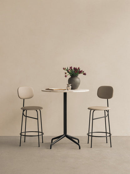 A marble-top Harbour Column Counter Table with a black star base, a vase of tulips and two Afteroom Counter Chairs.