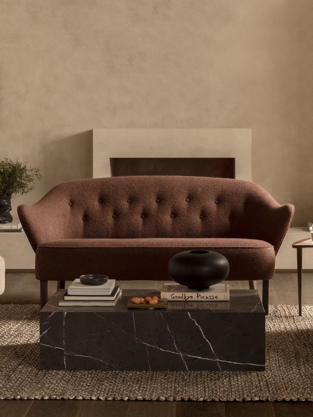 The Ingeborg Sofa in brown fabric shown in a living room with a black marble Plinth Low coffee table in front of a fireplace.